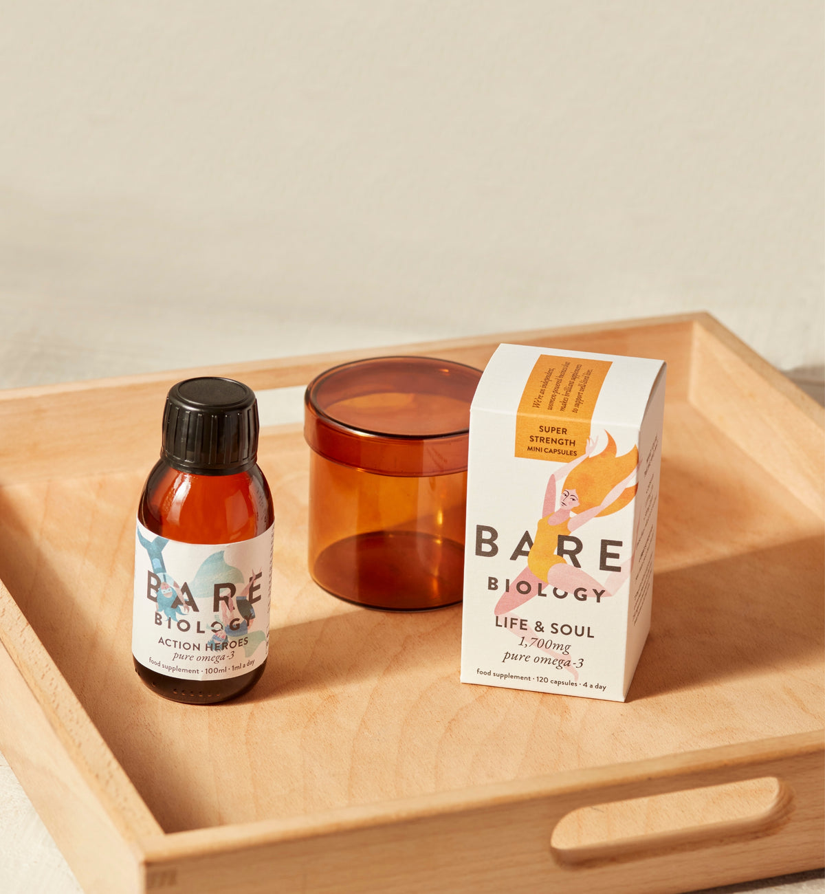 Bare Biology products including an Action Heroes Omega-3 bottle and box packaging of Omega-3 fish oil mini capsules displayed side by side on a wooden tray.
