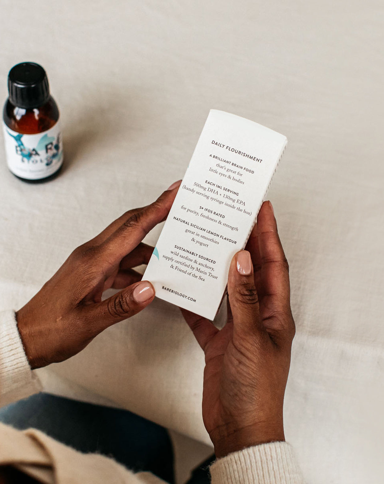 a woman holding bare biology action heroes omega 3 liquid for kids box