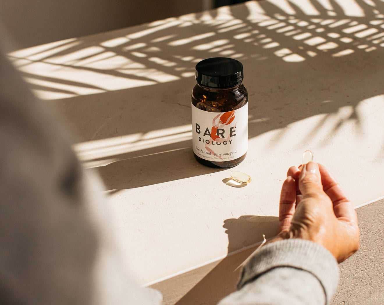 a woman holding life & soul daily omega-3 capsules in the sunshine