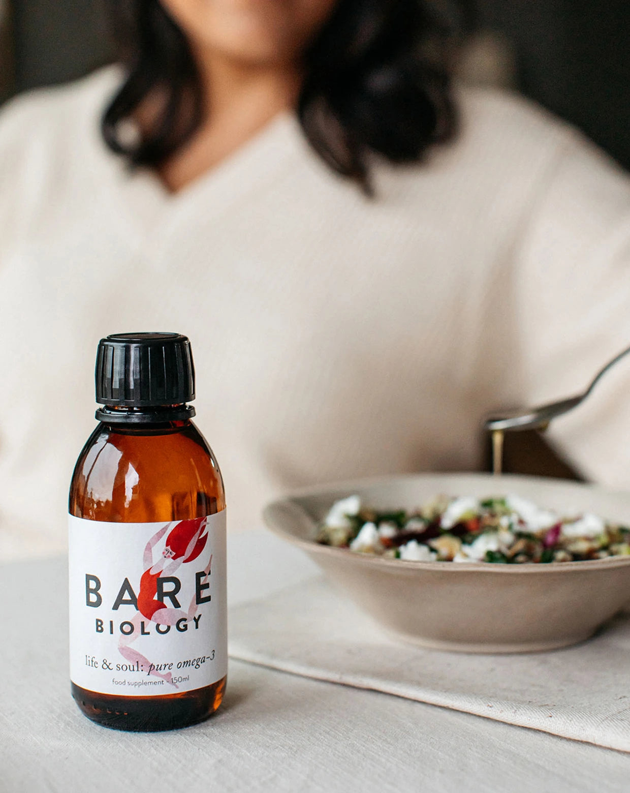 a woman pouring a teaspoon of life & soul omega 3 liquid onto a bowl of salad