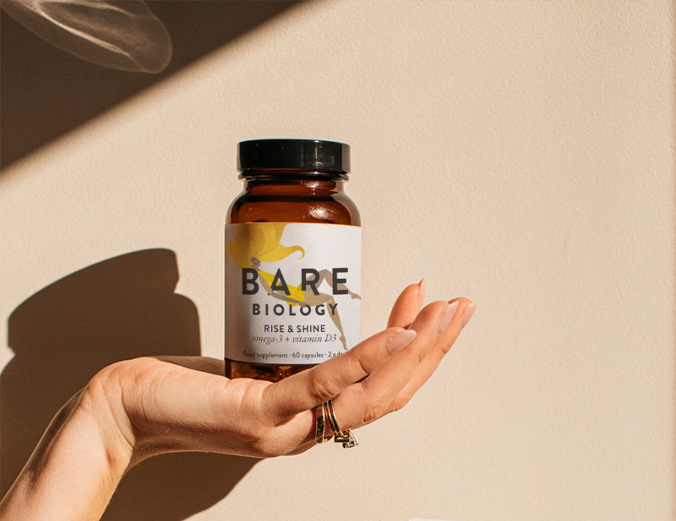 Hand holding a bottle labeled 'Bare Biology' on a beige background