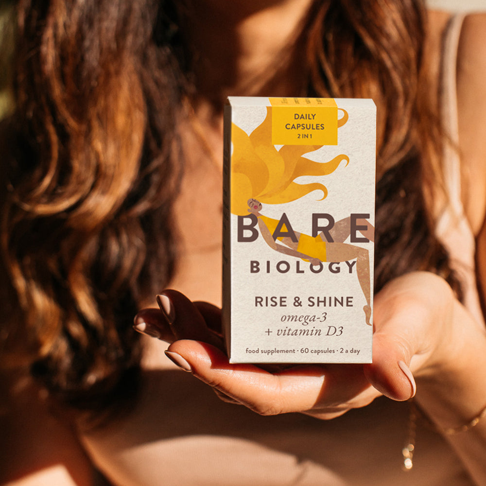 Person holding a box of Bare Biology Rise & Shine supplement with the Sun Shining in their direction