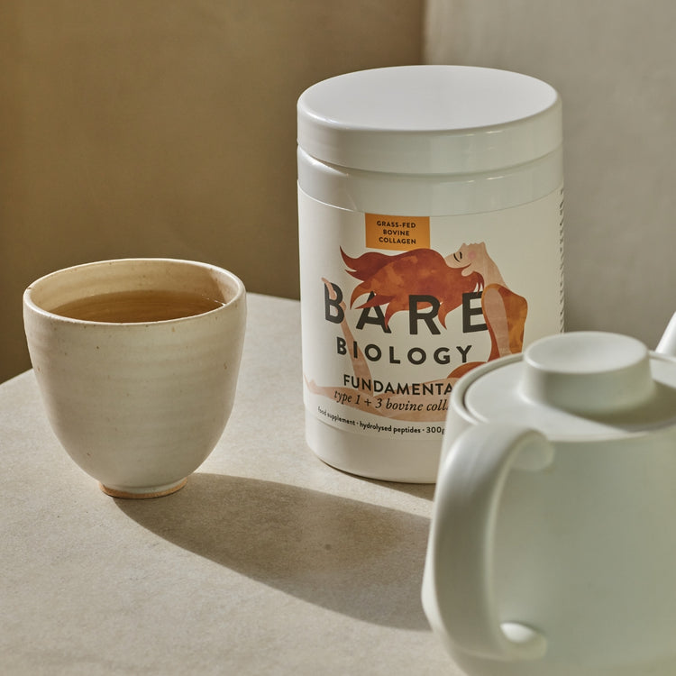 Bare Biology Fundamental Bovine Collagen tub positioned in between a cup of tea and a tea pot