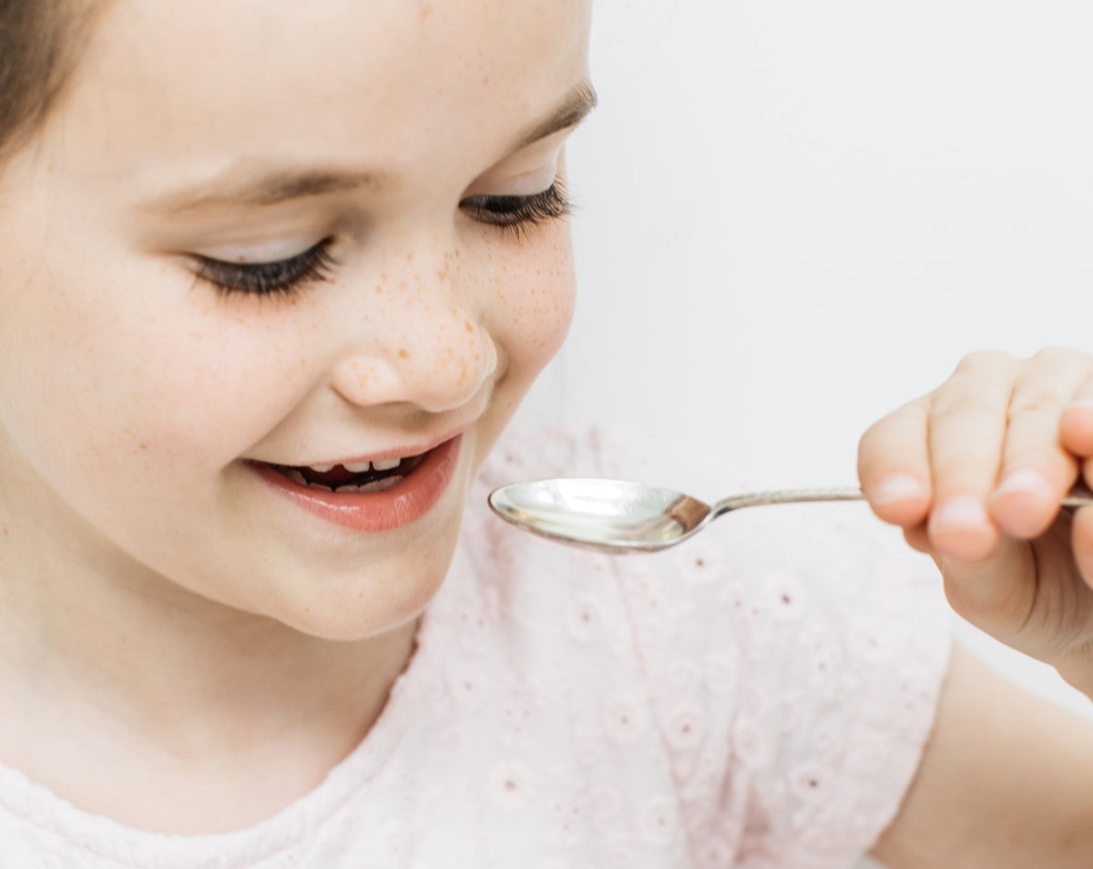 a kid holding a spoon of bare biology omega 3 high strength fish oil