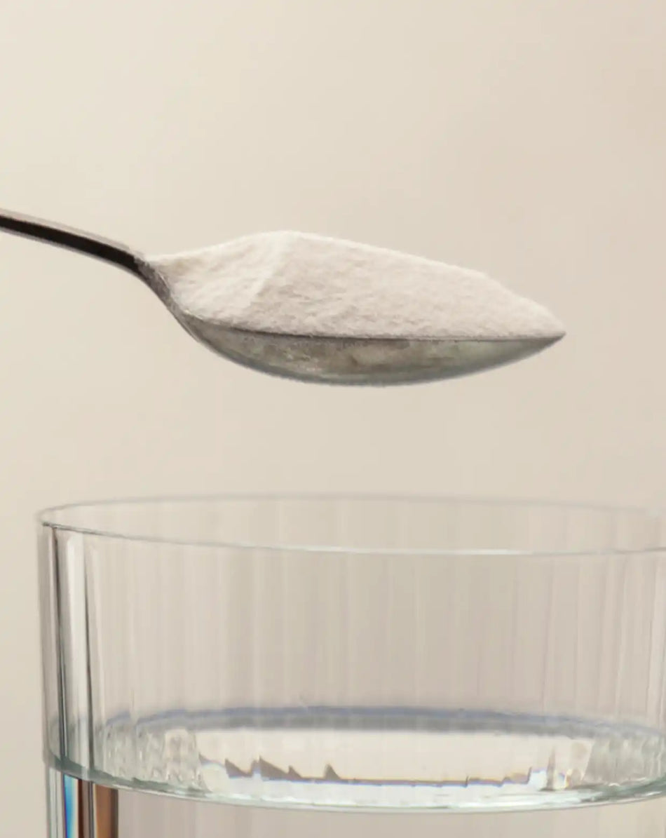 a spoon of collagen powder over a glass of water