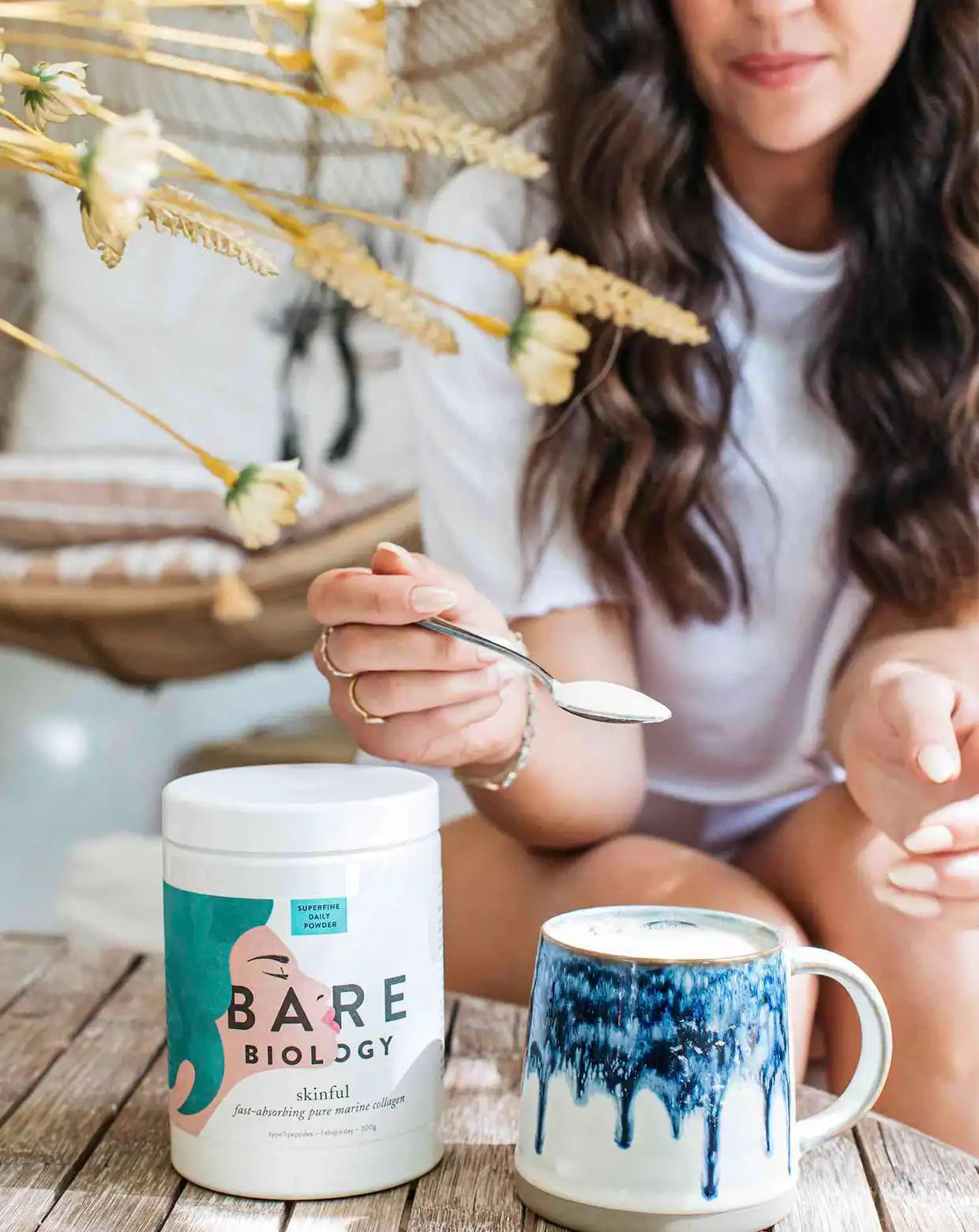 a woman holding a spoonful of marine collagen from bare biology above a cup of coffee