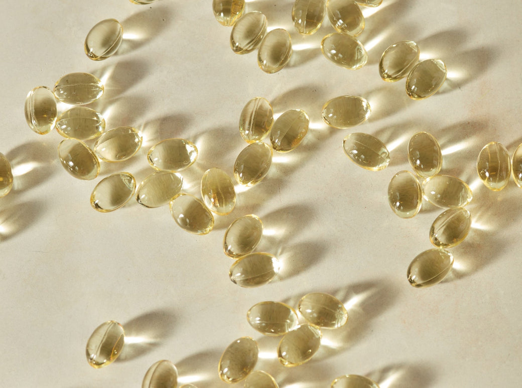 Yellow mini softgel capsules scattered on a light background surface