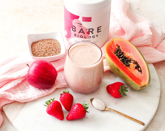 Bare Biology strawberry flavoured skinful marine collagen with vitamin c next to apple, papaya, strawberries and a smoothie, 