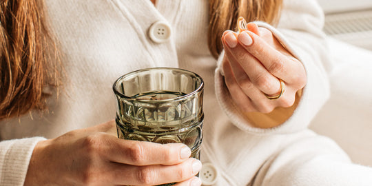 Woman holding Bare Biology omega-3 capsule and glass of water.