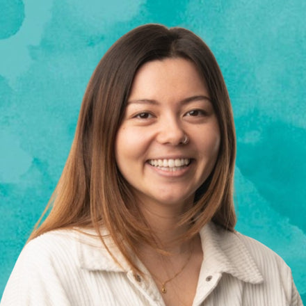 Woman with shoulder-length brunette hair smiling against a teal background