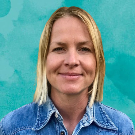 Woman with blonde hair wearing a denim shirt against a teal background