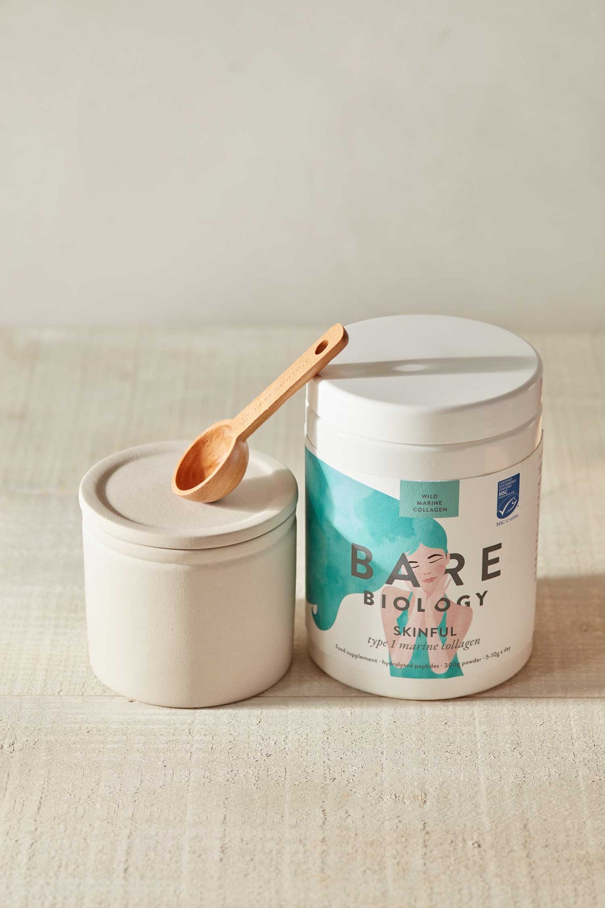 Container of Bare Biology Skinful Pure Marine collagen with a wooden spoon on a neutral background