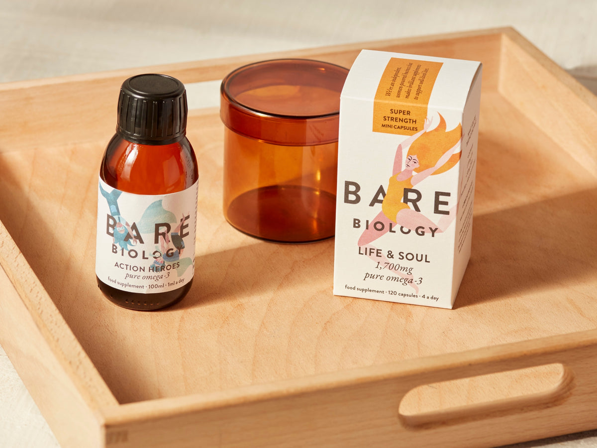 Bare Biology products including a bottle of kids fish oil and box of mini omega-3 capsules on a wooden tray.