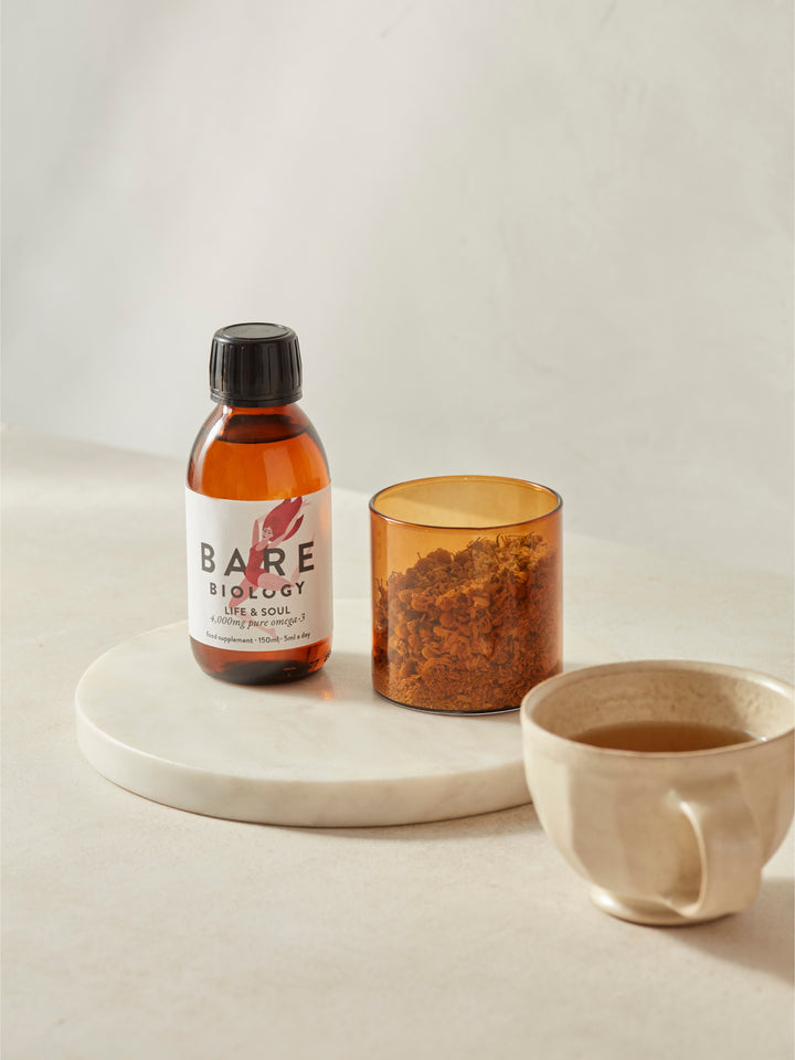 Bare Biology fish oil liquid glass bottle on a marble tray with a candle and mug on a light background