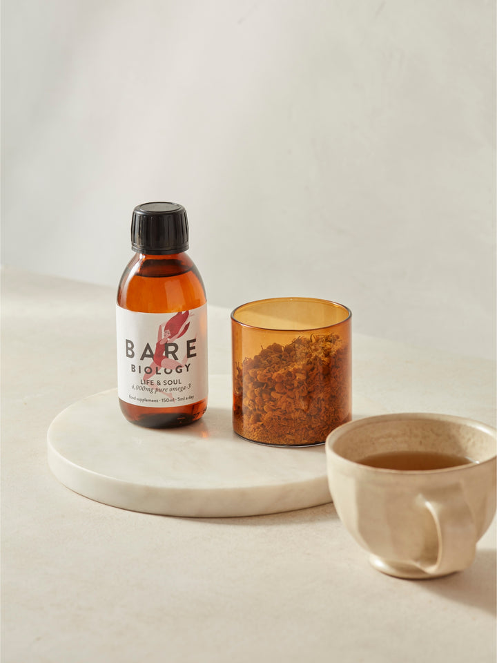 Bottle of Bare Biology Life and Soul Omega-3 fish oil Liquid on a marble tray with a cup and container on a light background