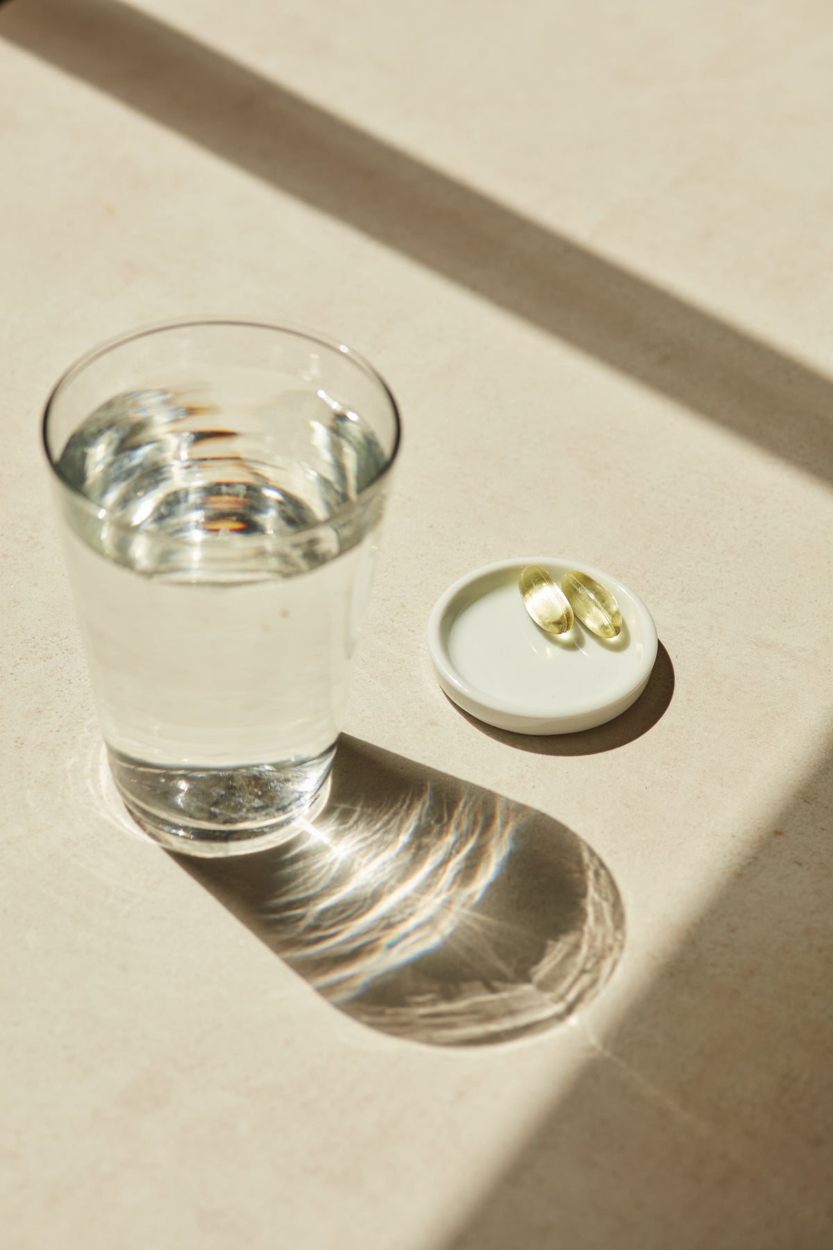 Clear glass of water next to a white coaster with two omega-3 life and soul daily capsules on a beige surface