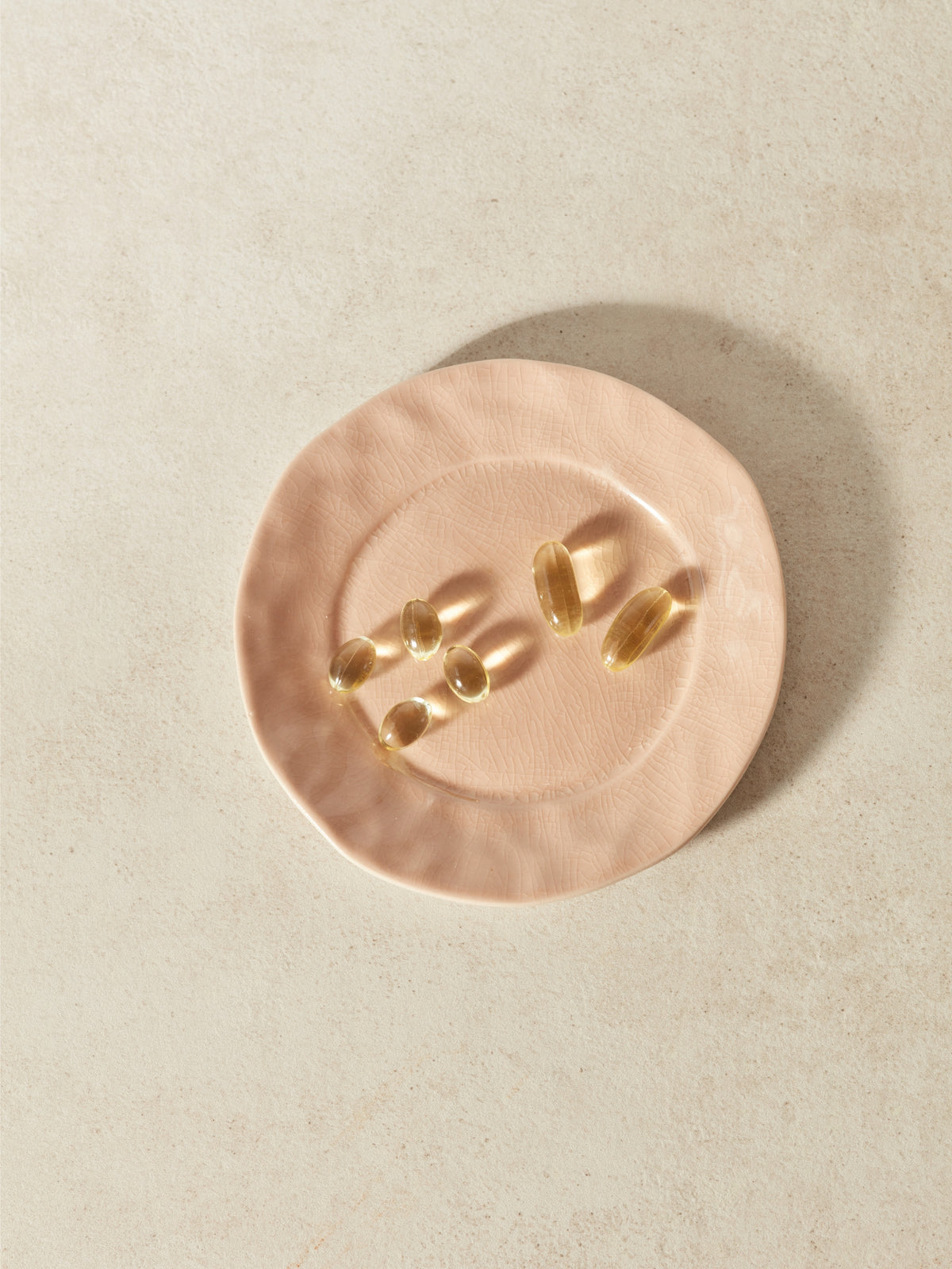 Six Omega-3 fish oil capsules displayed on a dusty pink ceramic dish against a beige background
