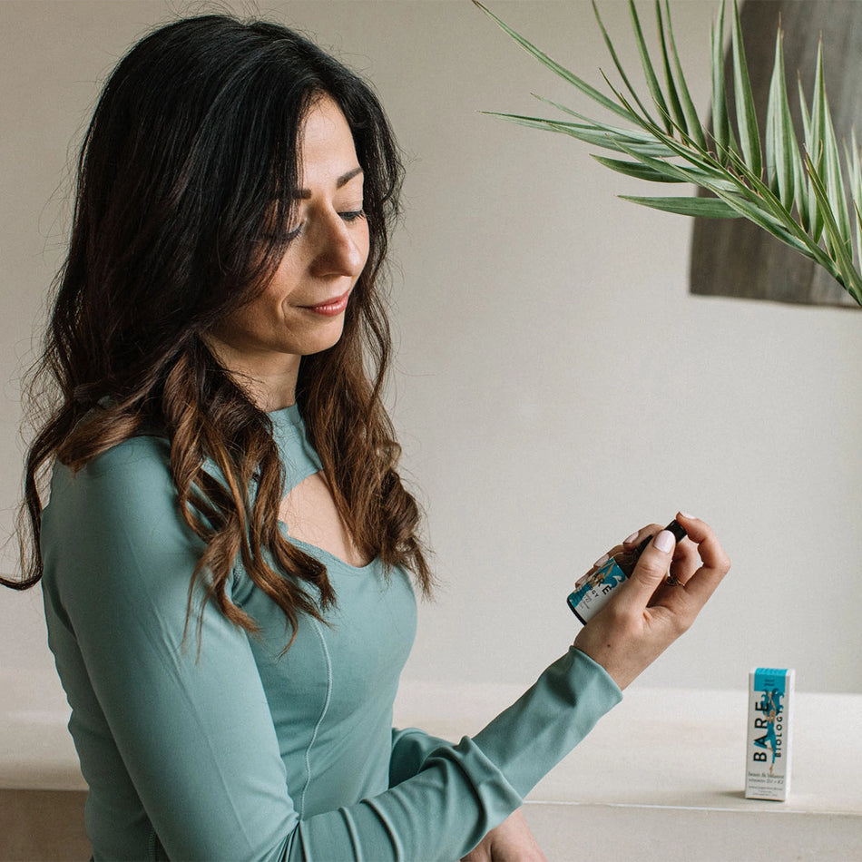 a woman in a teal workout set holding bare biology's beam & balance spray