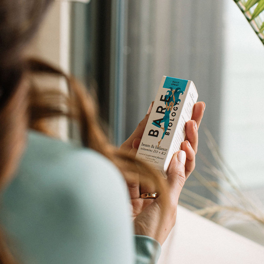 woman holding bare biology beam and balance vitamin d3 and k2 spray bottle