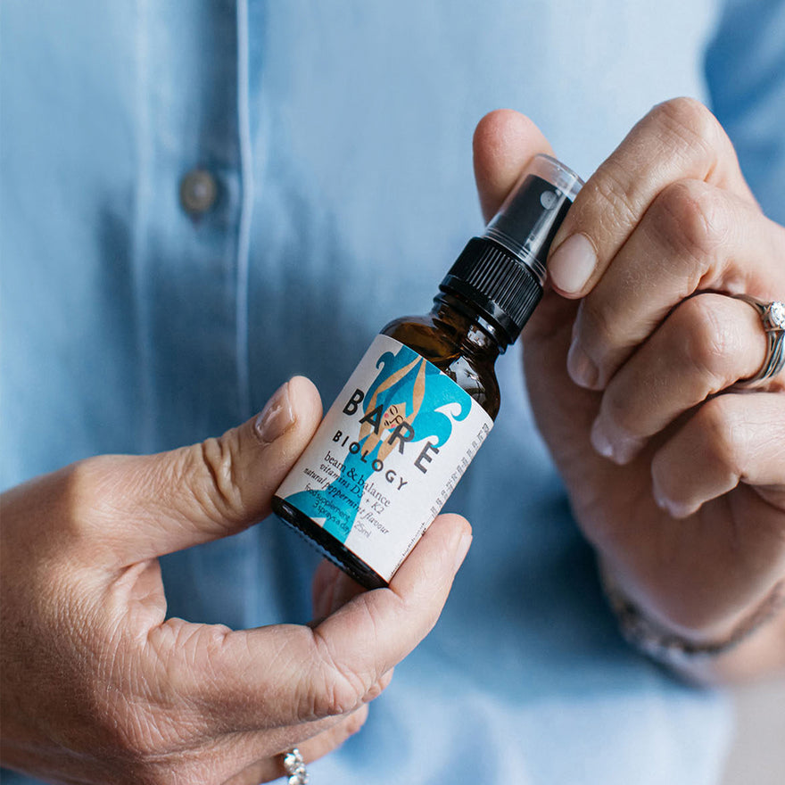 close up of a woman holding bare biology beam and balance vitamin d plus k2 spray