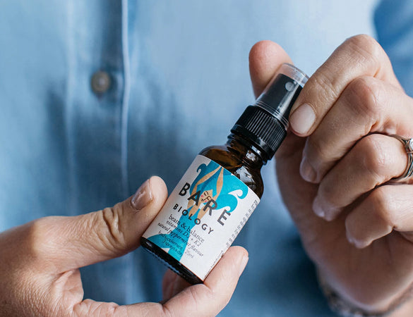 a woman in a blue shirt holding beam & balance vitamin d3 and k2 spray 