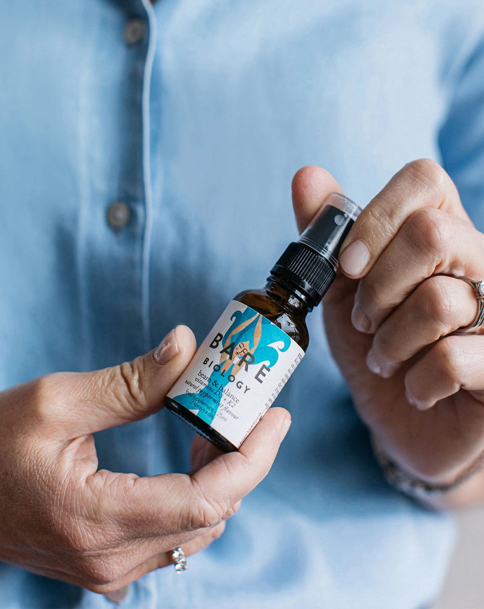 a woman in a blue shirt holding beam & balance vitamin d3 and k2 spray 