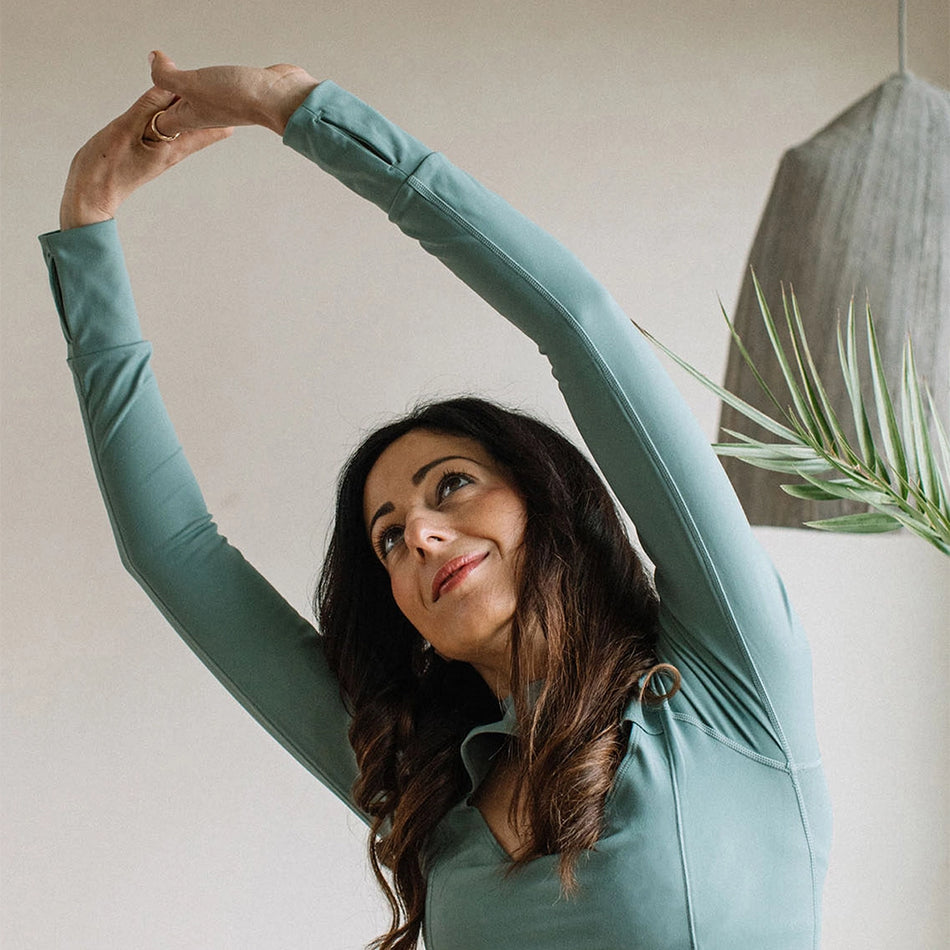 a woman stretching her arms over her head in a teal workout set