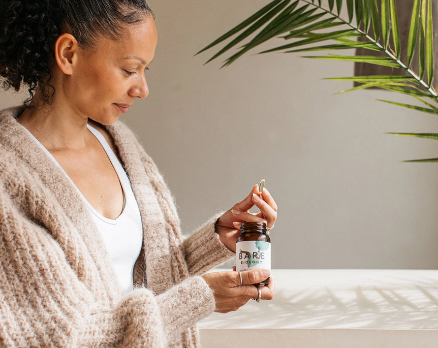 a woman holding a mindful omega 3 capsules in the sun next to a plant