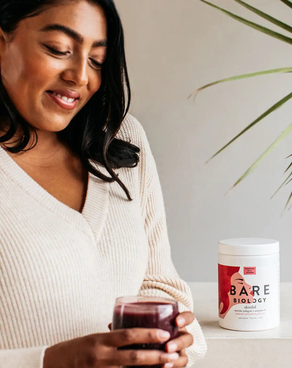 a woman holding a strawberry smoothie with bare biology skinful collagen powder + vitamin c