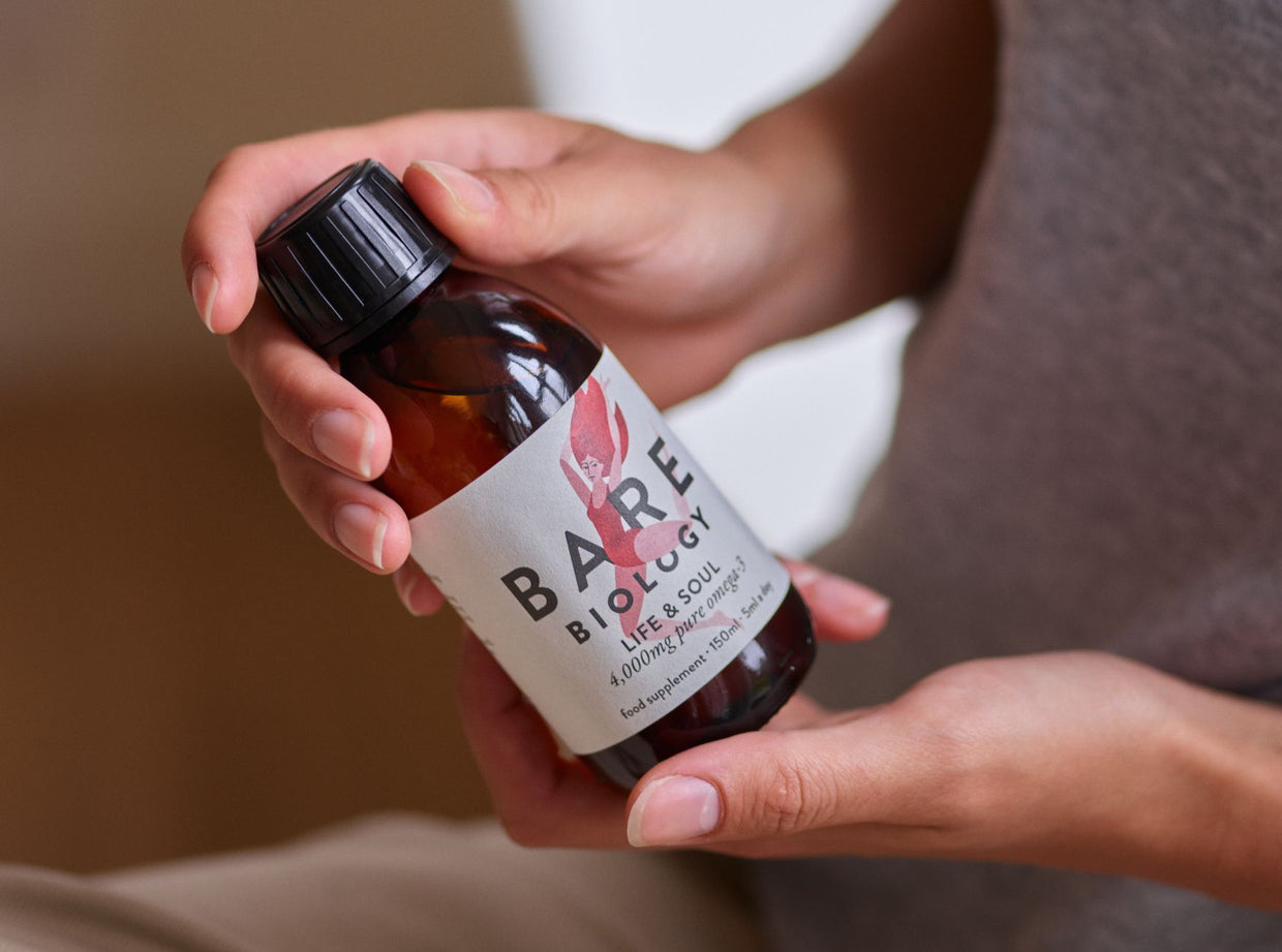 Hand holding a bottle labeled 'Bare Biology' with a blurred background