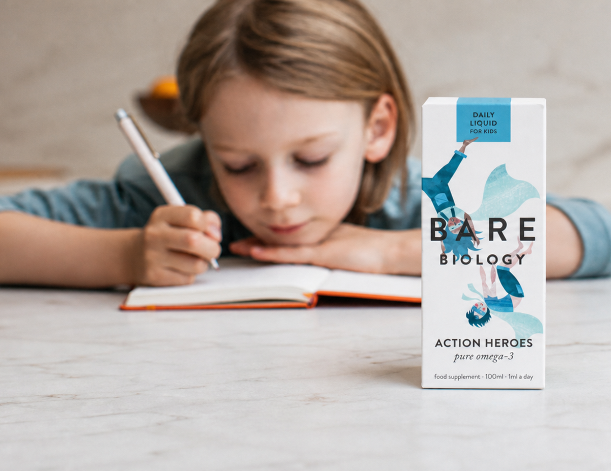 A child with their head on their school book, writing. There's a bottle of Action Heroes omega-3 fish oil in the foreground.