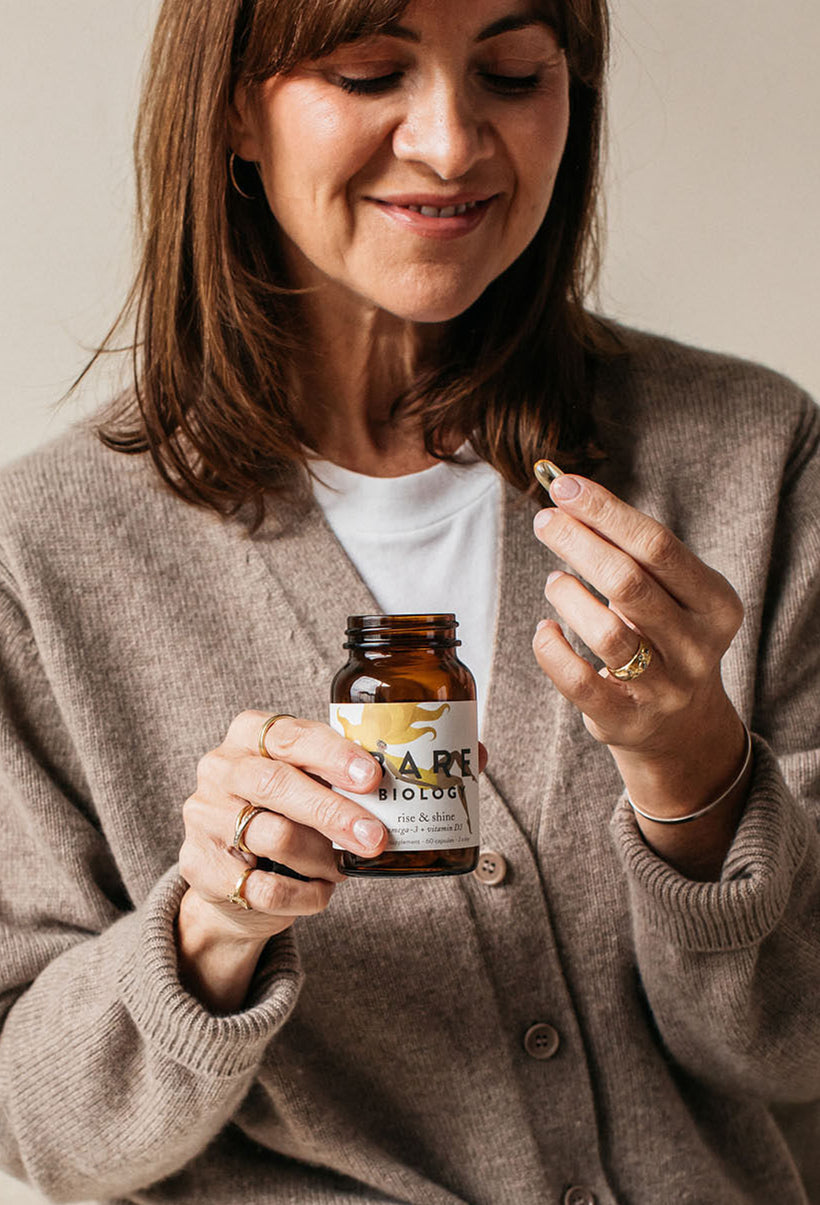 a woman holding and about to take a bare biology rise and shine omega 3 capsule