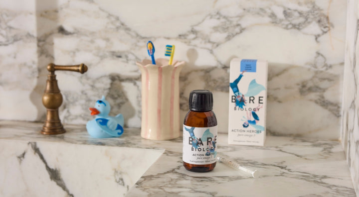 Bare Biology Kid's Omega-3 liquid product on a marble bathroom counter with a rubber duck and toothbrushes.