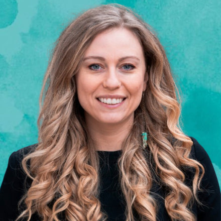 Woman with long, wavy hair smiling against a teal background