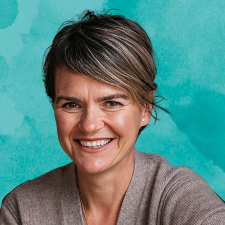 Woman with short brown hair smiling against a teal background