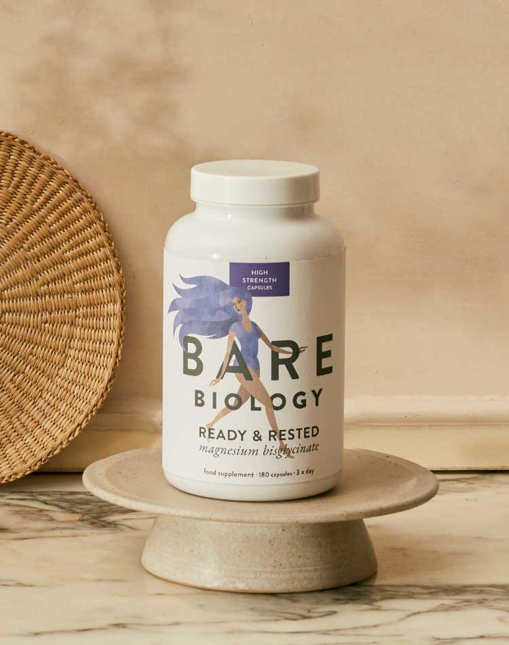 Bottle of Bare Biology magnesium supplement on a marble surface with a woven basket in the background