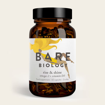 A brown glass bottle labeled Bare Biology contains Rise & Shine Omega-3 Plus Vitamin D3 capsules, featuring a yellow sun illustration. The label advises taking two capsules daily for optimal benefits.