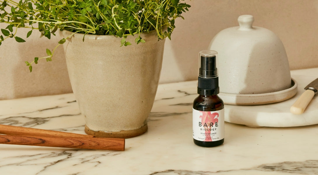 Bottle of Bare Biology Vitamin D spray on a marble surface with a plant and ceramic items in the background