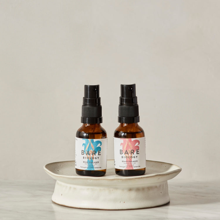 Two bottles of Bare Biology vitamin D spray on a white ceramic stand with a plain background.