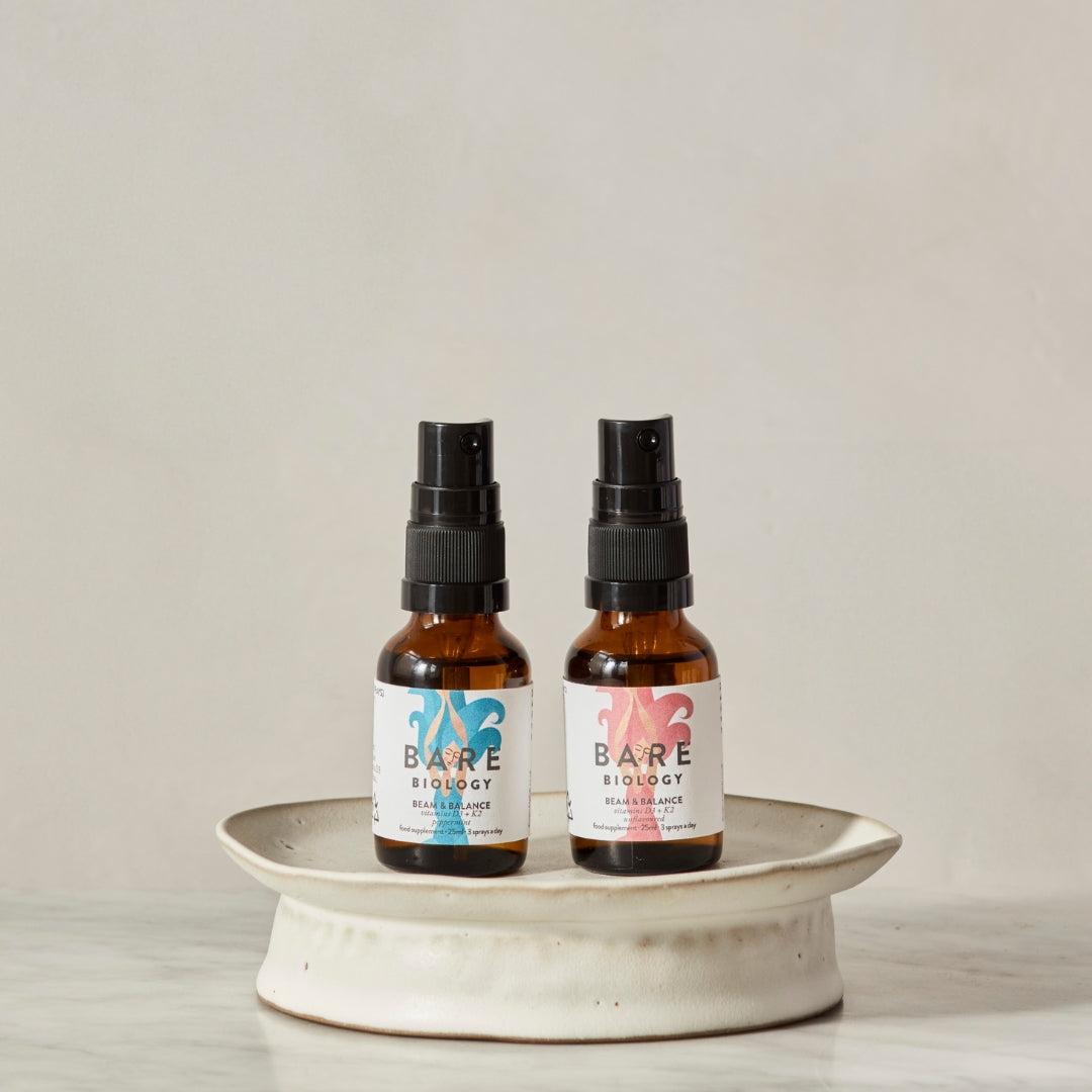 Two bottles of Bare Biology vitamin D spray on a white ceramic stand with a plain background.