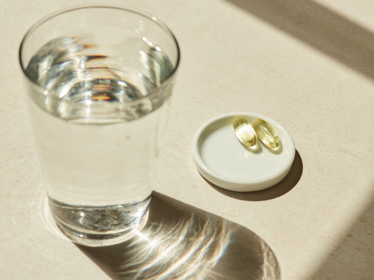 Two Rise and Shine capsules on a small white dish next to a clear glass on a beige surface.