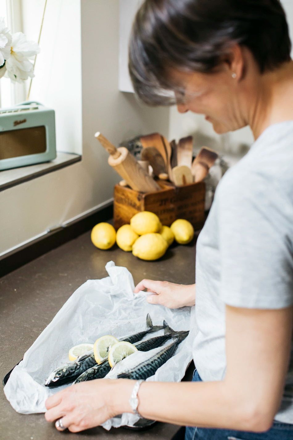 a woman preparing fish with lemon slices on a baking tray