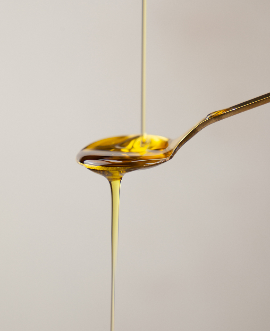 close up of omega-3 fish oil being poured onto a gold teaspoon and dripping off the spoon.
