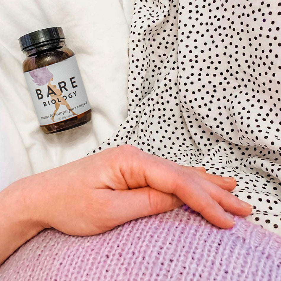 a woman holding her baby bump with mums & bumps pregnancy omega 3 capsules