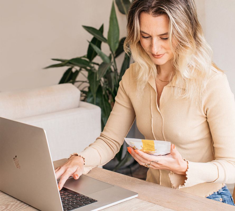 bare biology team holding rise & shine vitamin d3 + omega 3 high strength capsules pouch and typing on a laptop