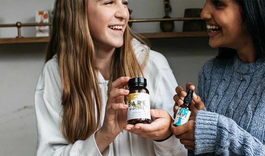 teenage girls holding bare biology rise and shine capsules and beam and balance vitamin d spray