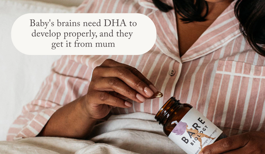 a woman in pink pyjamas holding bare biology omega 3 supplement for pregnancy in bed