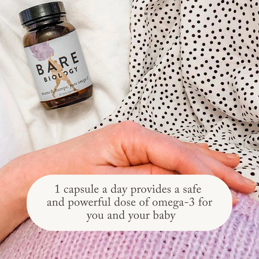a woman holding her baby bump with bare biology omega 3 supplement for pregnancy on the bed next to her