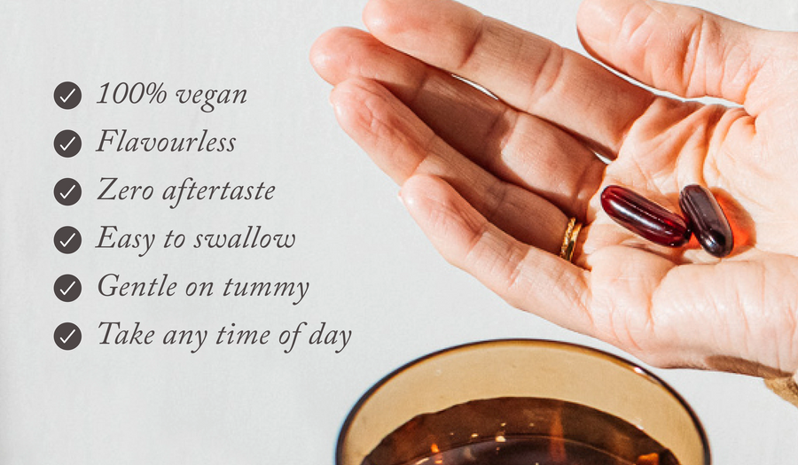 2 bare biology vim & vigour vegan omega 3 capsules in a hand with a glass of water in orange glass