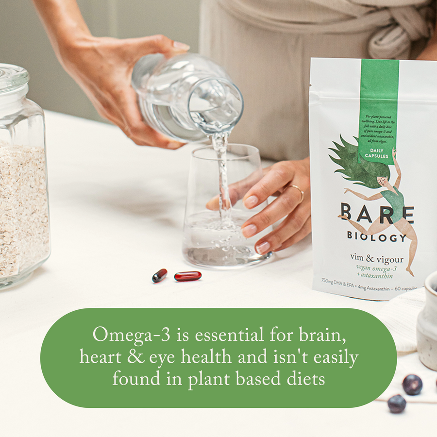bare biology vim & vigour vegan omega 3 pouch and capsules on a kitchen table with a bowl of blueberries and a woman pouring a glass of water